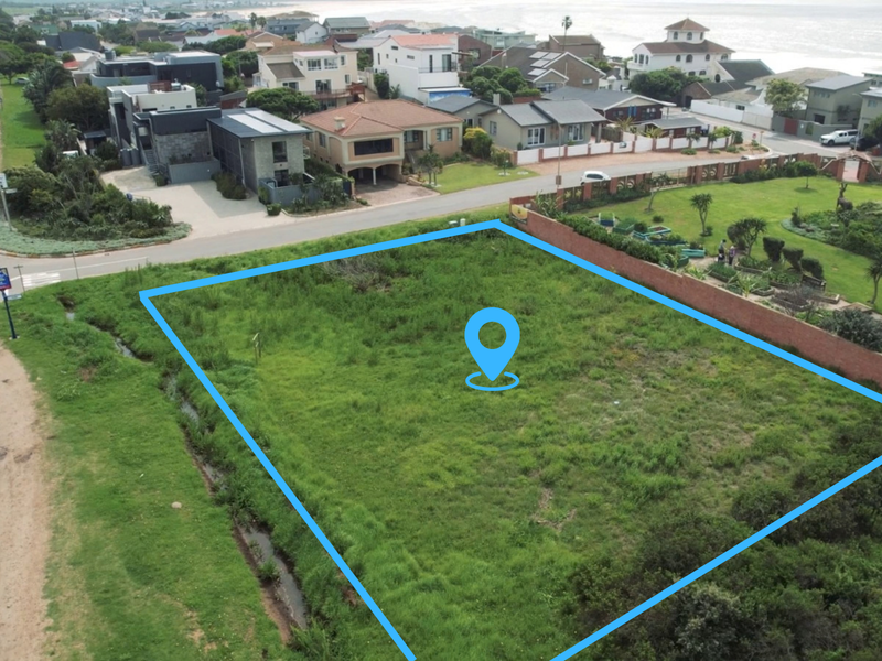 An aerial view of a vacant residential plot situated in a coastal neighborhood, featuring grass cover and proximity to existing residential properties.