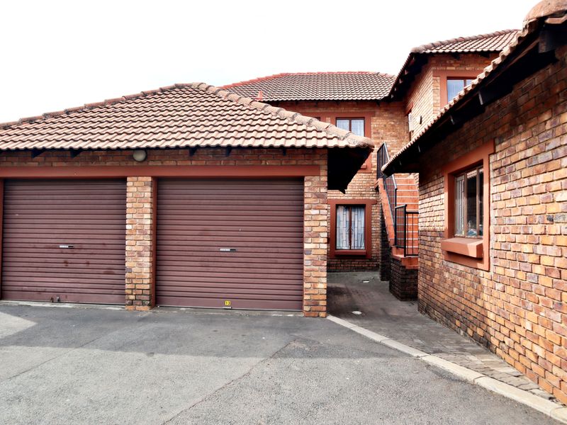 Exterior view of a facebrick apartment complex featuring a double garage with roller doors and an external staircase leading to upper levels.