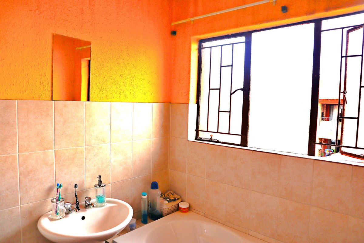 A compact bathroom featuring a pedestal basin, tiled splashback, and a window with security bars, requiring cosmetic updates to improve its overall condition.