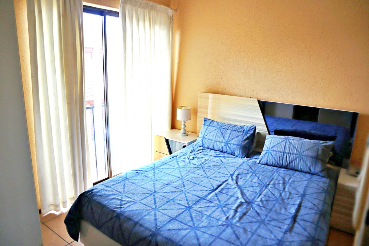 A bedroom featuring tiled flooring and a sliding glass door providing access to a balcony, with a built-in headboard.