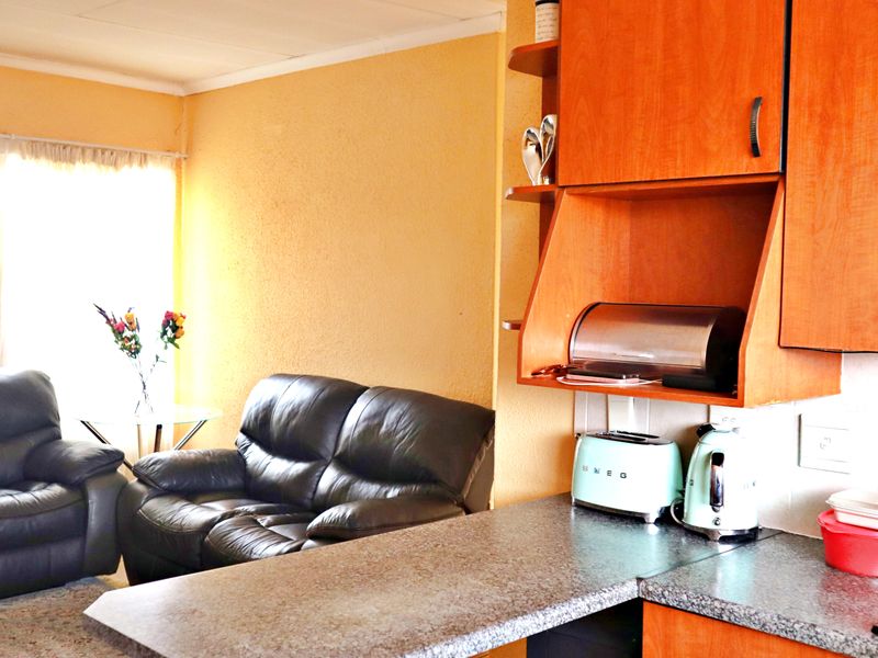 Open plan living area featuring a compact kitchen with laminate cabinetry and a breakfast counter, seamlessly flowing into the adjacent lounge space.