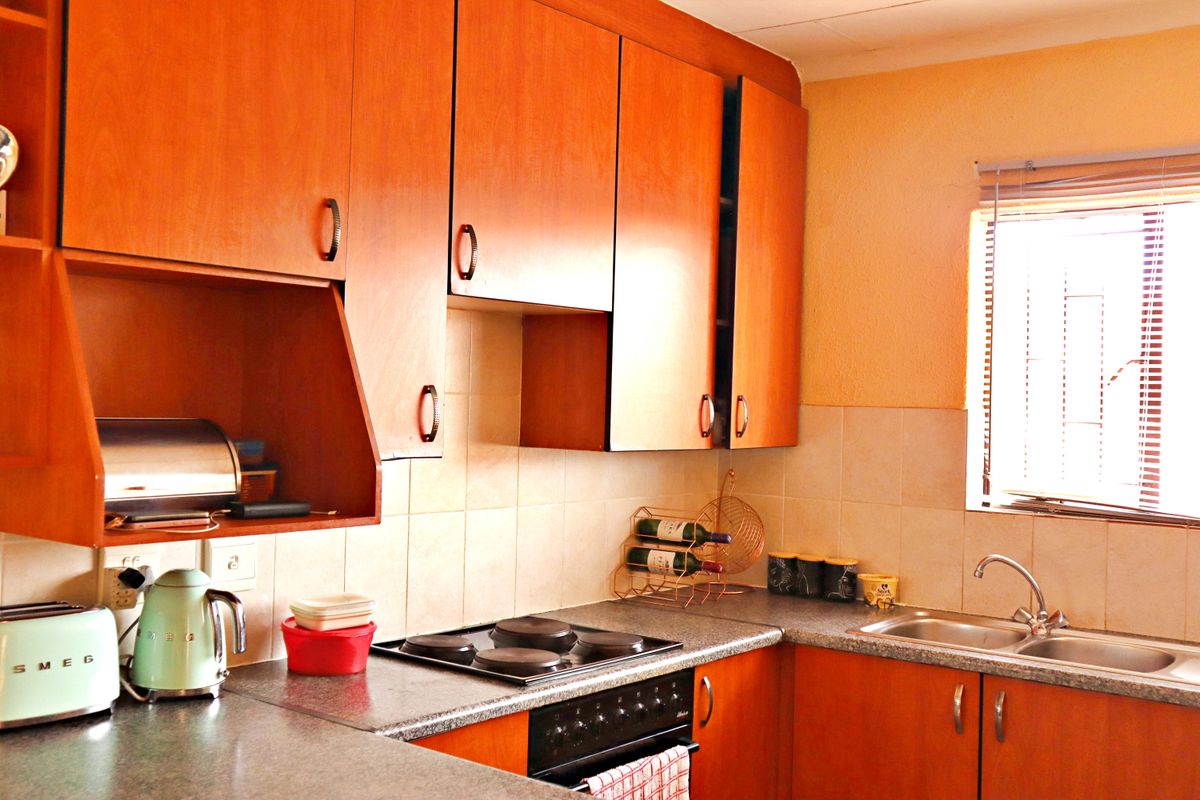 A functional kitchen featuring wood-look laminate cabinetry, a tiled backsplash, built-in electric cooking appliances, and a stainless steel double sink with a window view.