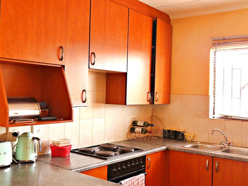 A functional kitchen featuring wood-look laminate cabinetry, a tiled backsplash, built-in electric cooking appliances, and a stainless steel double sink with a window view.