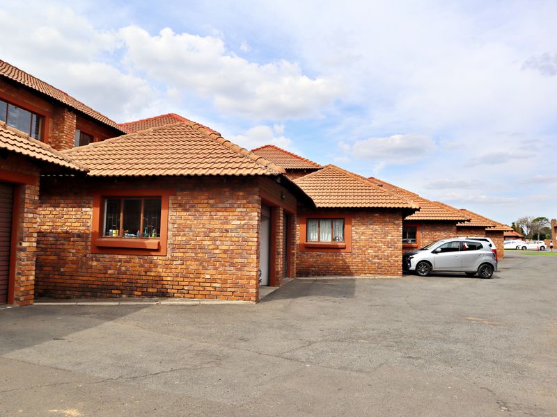 Exterior view of a face brick apartment complex featuring tiled roofing, garage access, and an asphalt driveway.