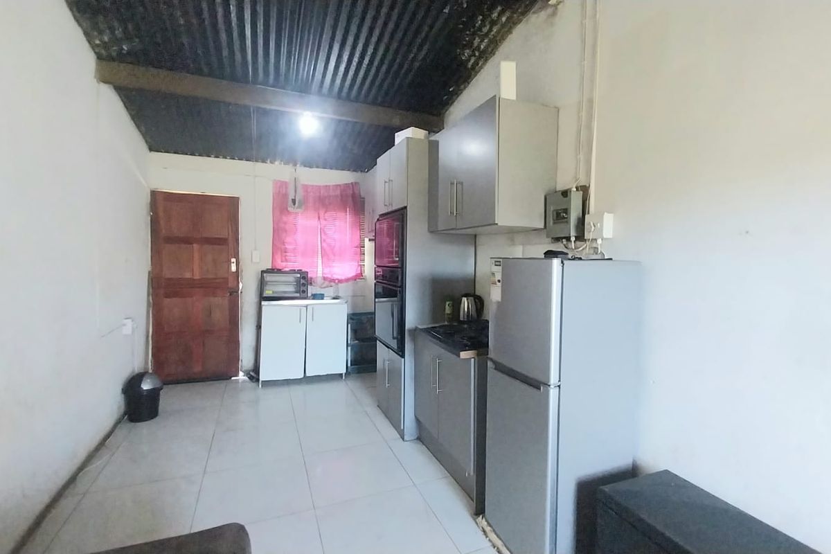 A functional kitchen area featuring built-in cabinetry, tiled flooring, and a corrugated metal ceiling, offering potential for cosmetic updates and modernization.