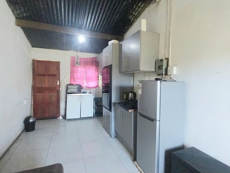 A functional kitchen area featuring built-in cabinetry, tiled flooring, and a corrugated metal ceiling, offering potential for cosmetic updates and modernization.