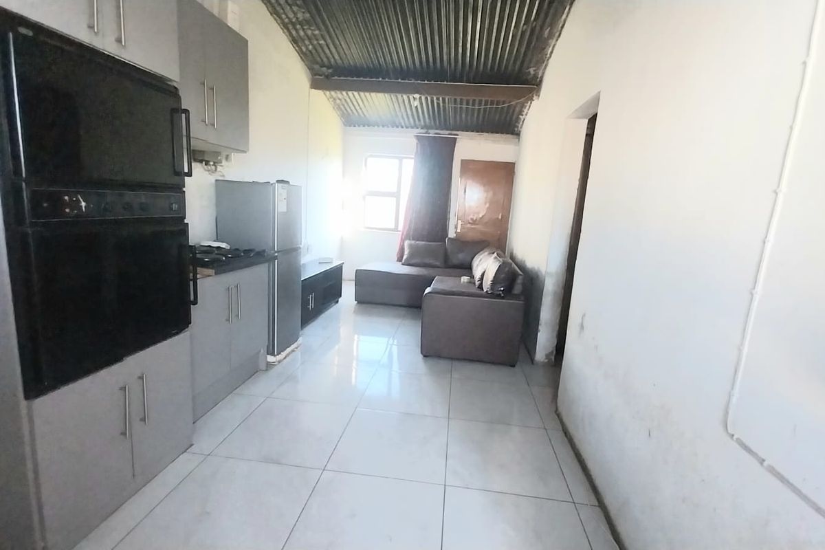 Open-plan living and kitchen area featuring tiled floors, built-in cabinetry, and an exposed corrugated metal ceiling, requiring cosmetic updates to the walls.