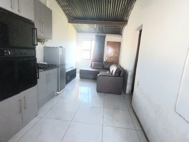 Open-plan living and kitchen area featuring tiled floors, built-in cabinetry, and an exposed corrugated metal ceiling, requiring cosmetic updates to the walls.