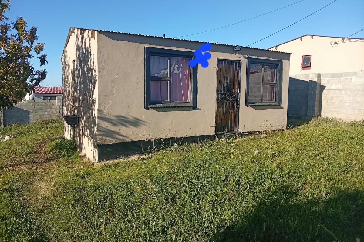 A detached structure featuring plastered walls, a corrugated metal roof, and security gate access, situated on a grassed plot.