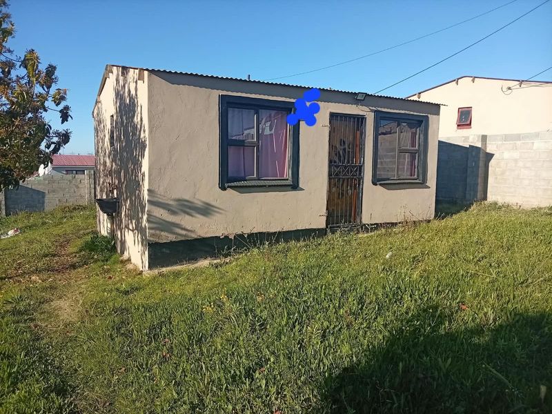 A detached structure featuring plastered walls, a corrugated metal roof, and security gate access, situated on a grassed plot.