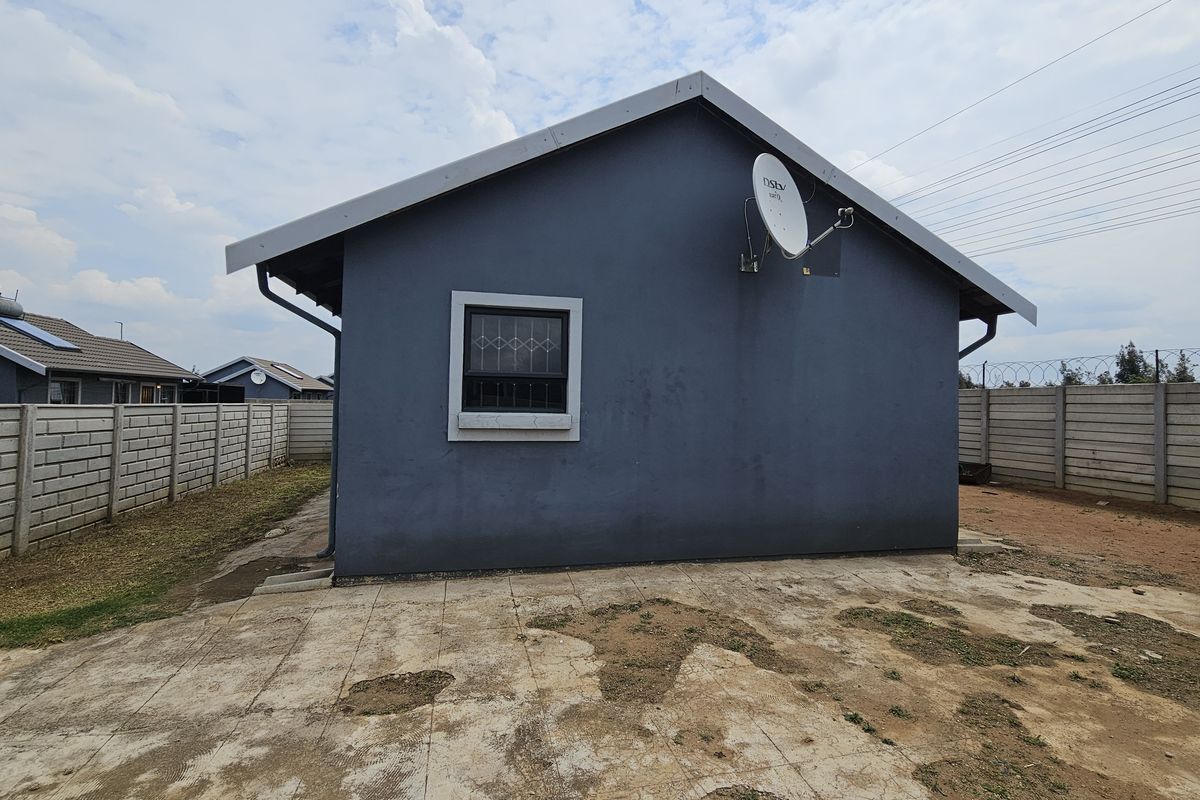 Rear view of the house featuring a concrete paved area, precast boundary walls, and a satellite dish mounted on the exterior wall.