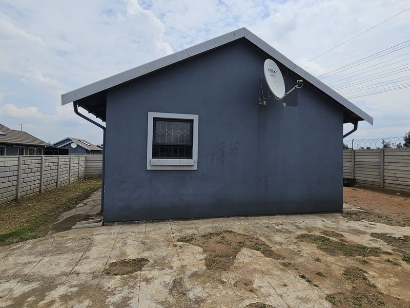 Rear view of the house featuring a concrete paved area, precast boundary walls, and a satellite dish mounted on the exterior wall.