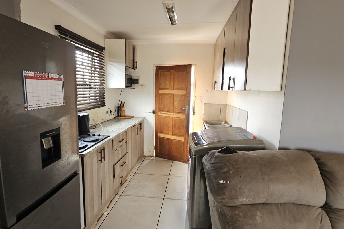 A functional kitchen featuring built-in cabinetry, laminate countertops, a hob, and tiled flooring, with direct access to an exterior timber door.