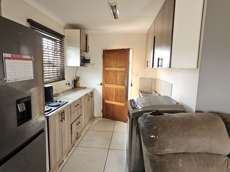 A functional kitchen featuring built-in cabinetry, laminate countertops, a hob, and tiled flooring, with direct access to an exterior timber door.