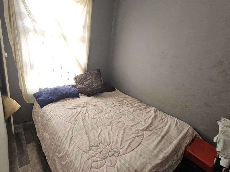 A compact bedroom featuring laminate flooring and a built-in cupboard, requiring cosmetic updates to the wall finishes.