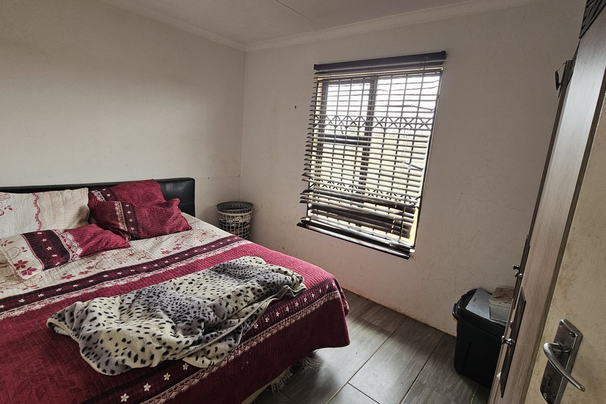 A bedroom featuring tiled flooring and a window with venetian blinds, showing signs of wear on the wall surfaces.