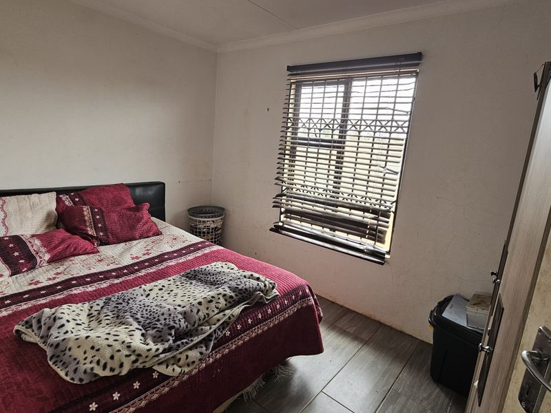 A bedroom featuring tiled flooring and a window with venetian blinds, showing signs of wear on the wall surfaces.