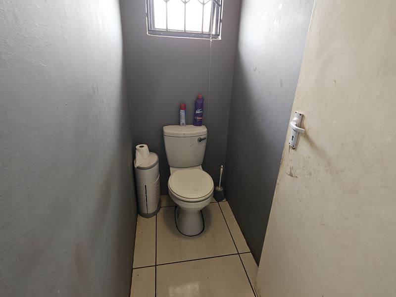 A compact bathroom featuring a standard toilet, tiled flooring, and a small window with security bars.