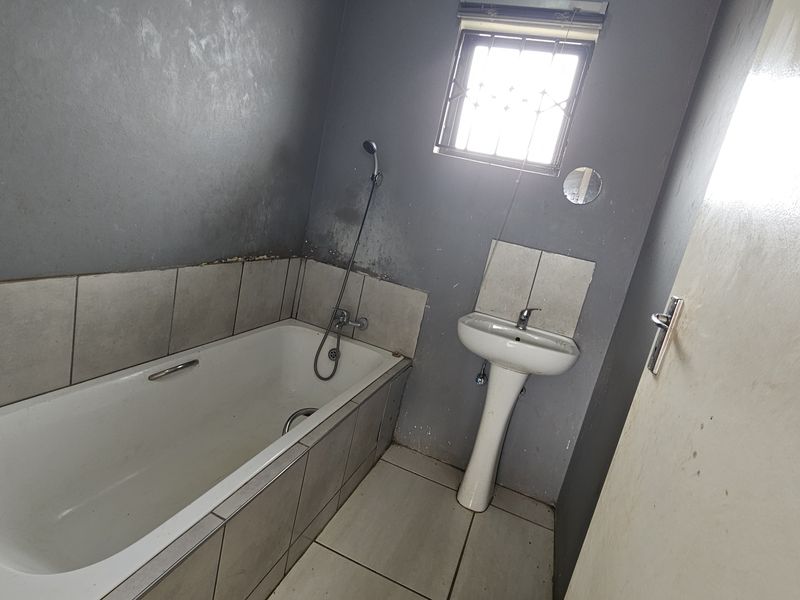 A functional bathroom featuring a bathtub, pedestal basin, and tiled finishes, currently requiring cosmetic updates to the wall surfaces.