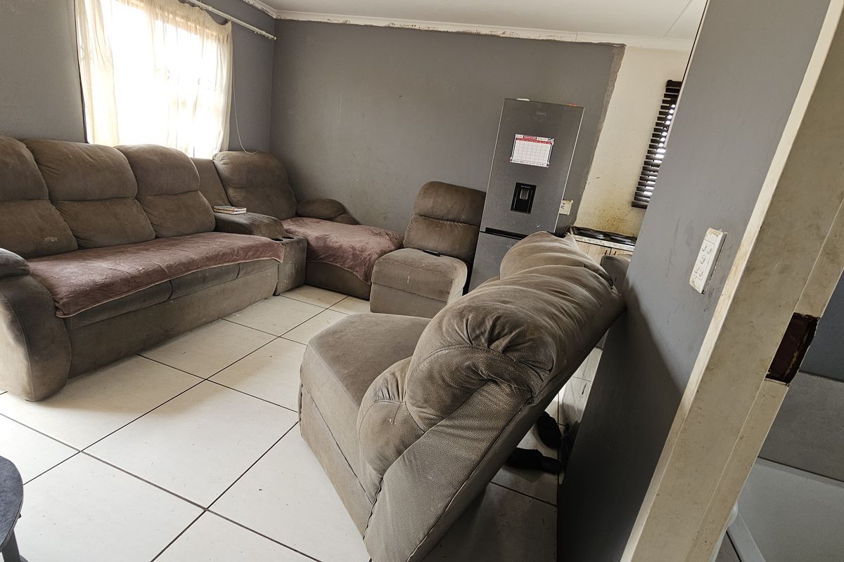 A living room area featuring tiled flooring and grey walls in need of maintenance and cosmetic updates.