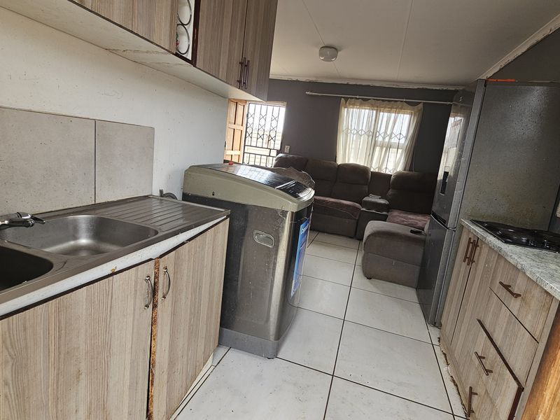 Open-plan kitchen and living area featuring wood-look cabinetry, tiled flooring, and a functional layout, offering potential for modernization and aesthetic improvement.