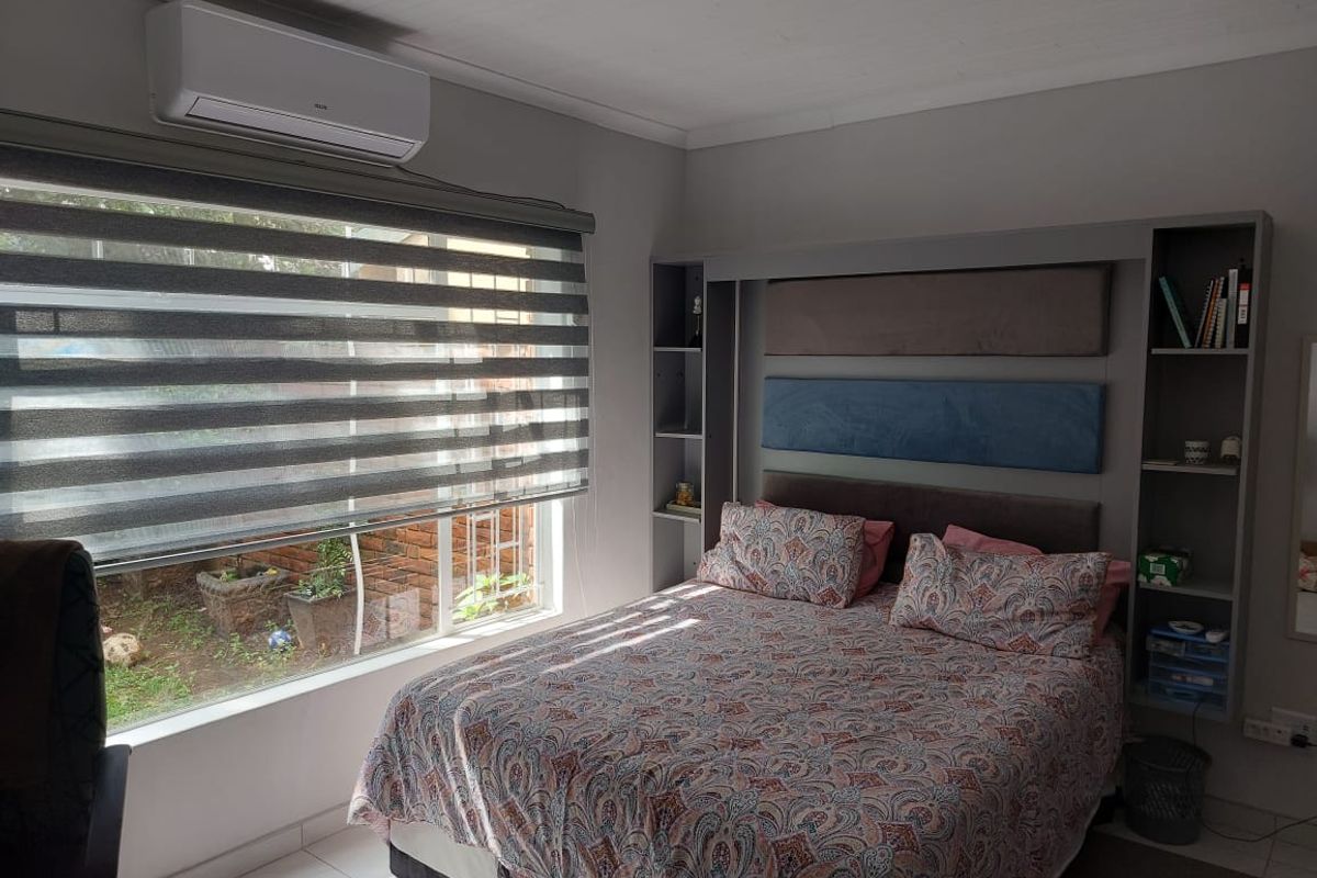 A well-maintained bedroom featuring a built-in headboard with integrated shelving, a split-system air conditioner, and modern roller blinds.