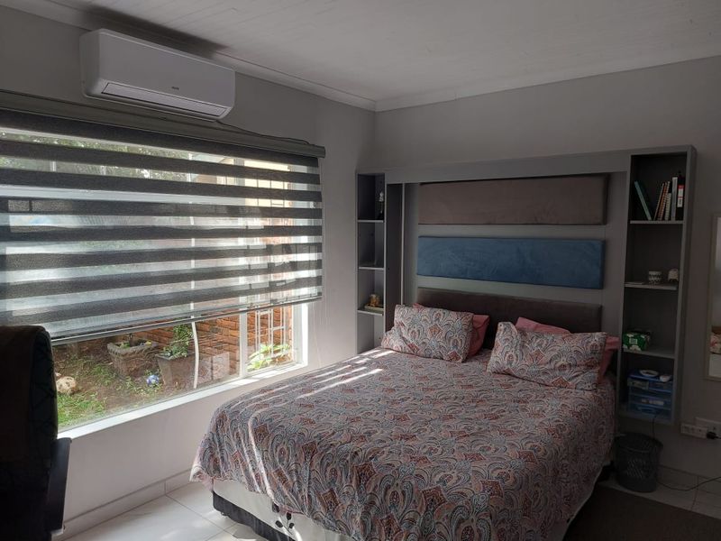 A well-maintained bedroom featuring a built-in headboard with integrated shelving, a split-system air conditioner, and modern roller blinds.