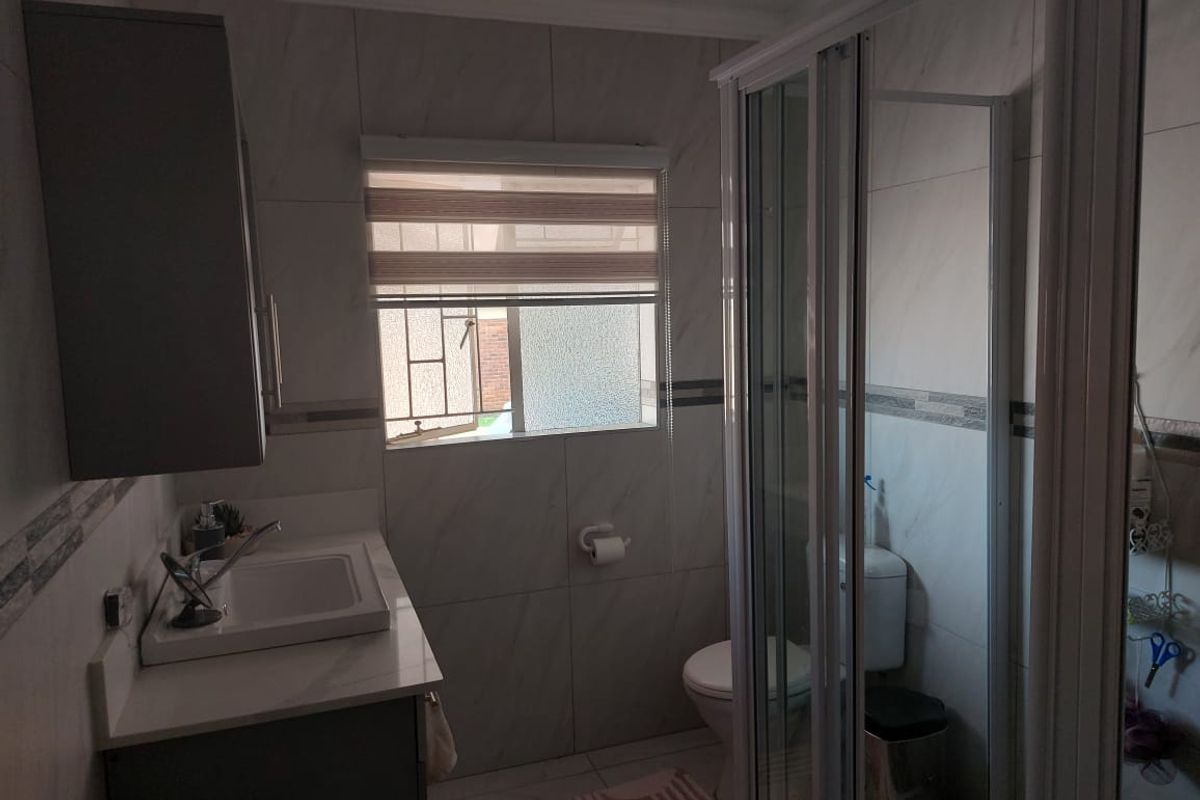 A functional bathroom featuring a vanity with basin, a glass-enclosed shower, and a toilet, finished with neutral wall tiling.
