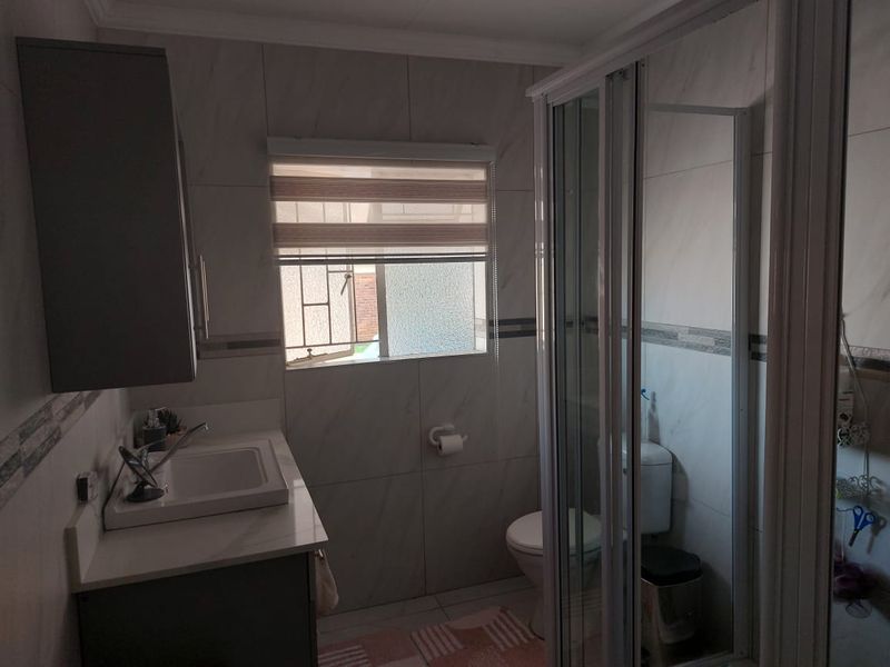 A functional bathroom featuring a vanity with basin, a glass-enclosed shower, and a toilet, finished with neutral wall tiling.