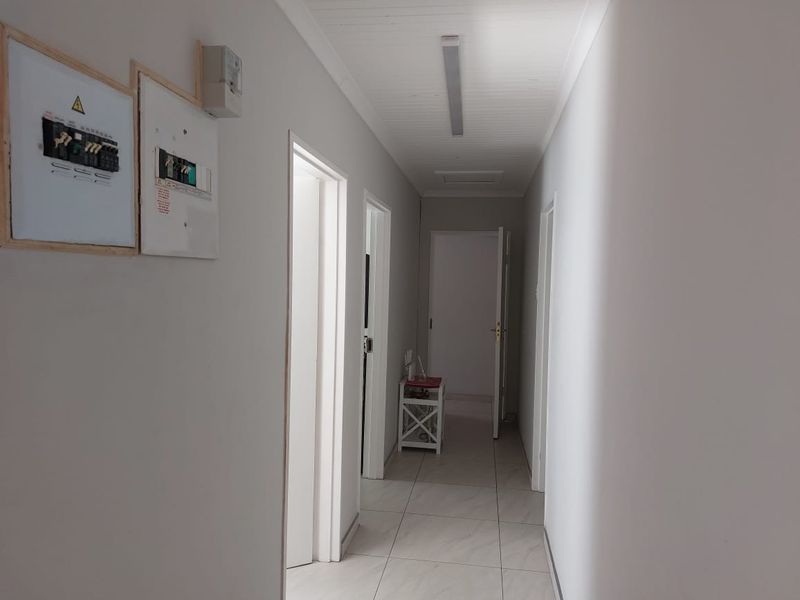 A clean, neutral hallway featuring tiled flooring, ceiling paneling, and a wall-mounted electrical distribution board, providing access to multiple rooms.