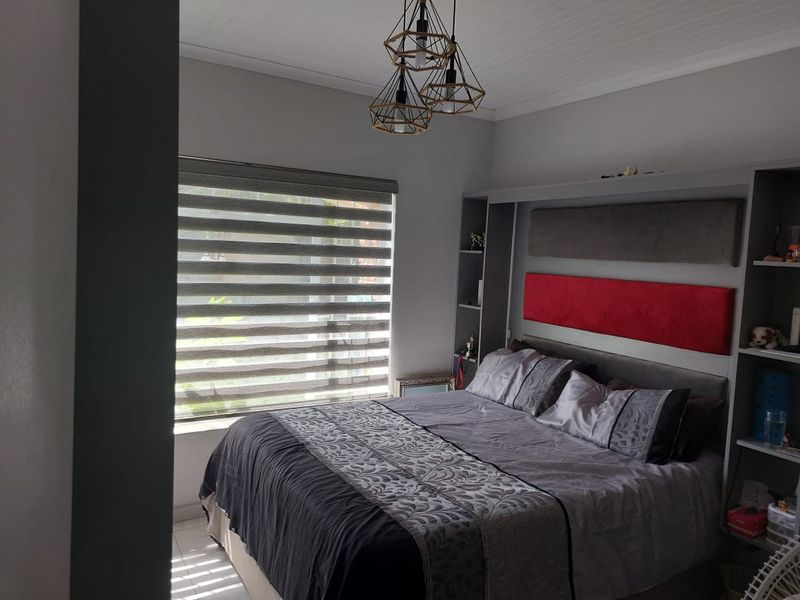 A well-maintained bedroom featuring built-in shelving, a custom upholstered headboard, and modern roller blinds, providing a functional and comfortable living space.