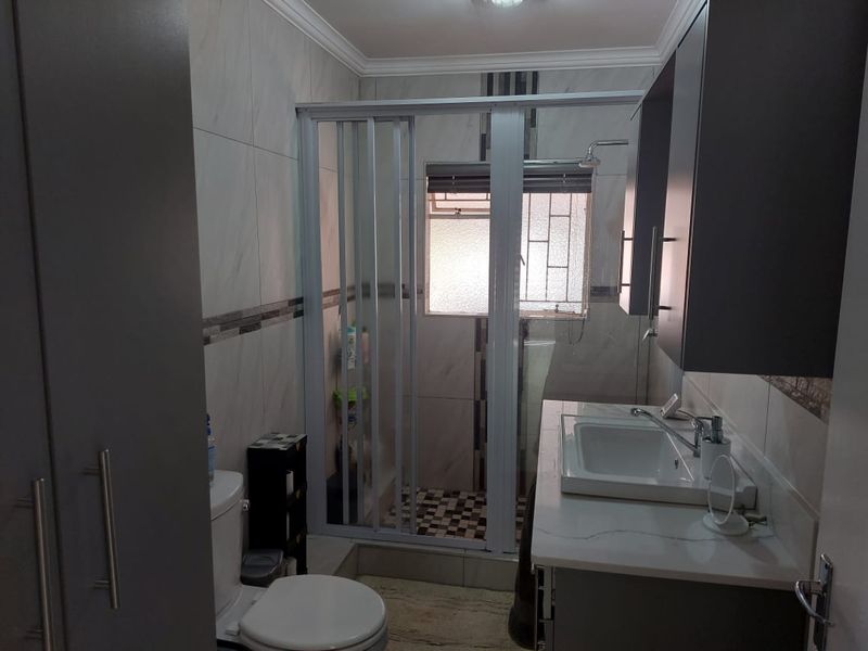 A modern bathroom featuring a shower enclosure, vanity cabinet with basin, and tiled walls.