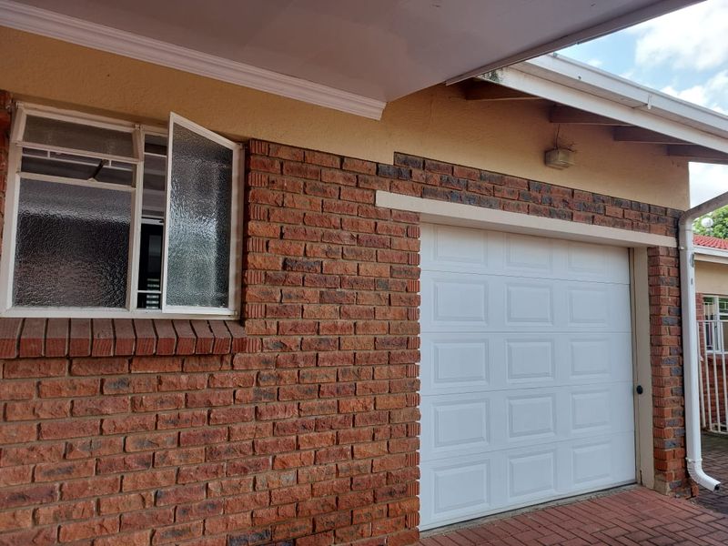 Exterior view of the townhouse featuring a face brick facade, a white sectional garage door, and a paved driveway area.