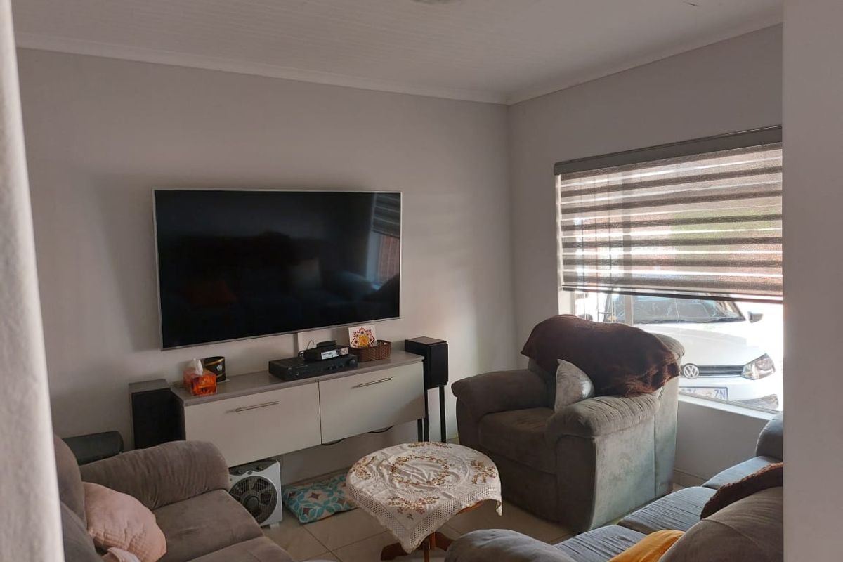 A comfortable living room featuring tiled flooring, neutral wall tones, and roller blinds, providing a functional and well-lit space for relaxation.