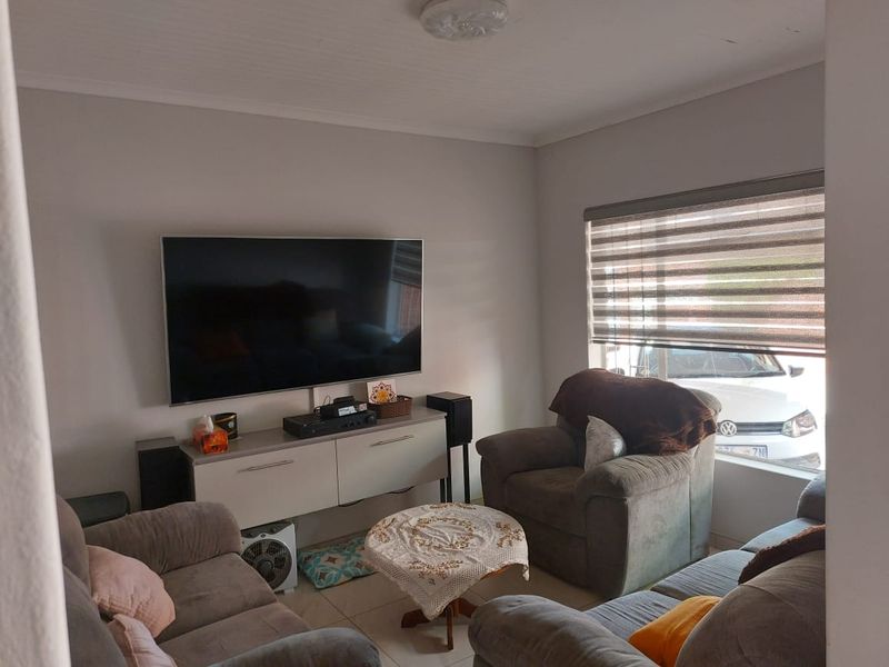 A comfortable living room featuring tiled flooring, neutral wall tones, and roller blinds, providing a functional and well-lit space for relaxation.