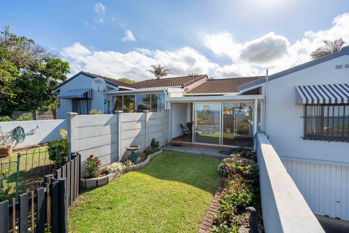 Rear exterior view of the townhouse featuring a small private garden, paved patio area, and sliding glass doors leading into the living space.