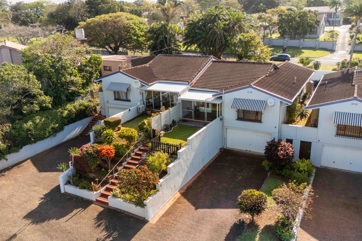 Aerial view of a townhouse complex featuring paved driveways, tiled roofs, and landscaped terraced gardens with retaining walls.