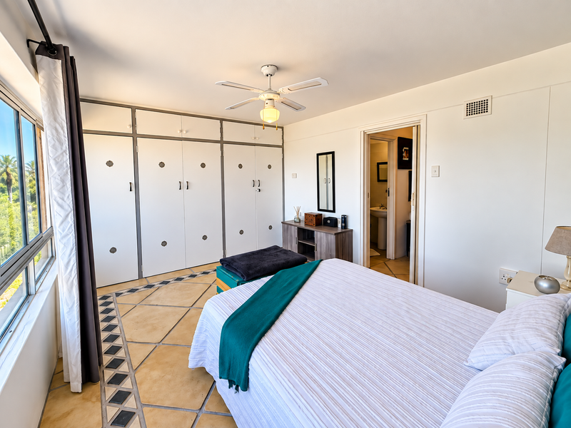 Spacious bedroom featuring built-in cupboards, a ceiling fan, and unique tiled flooring, with direct access to an en-suite bathroom and large window views.