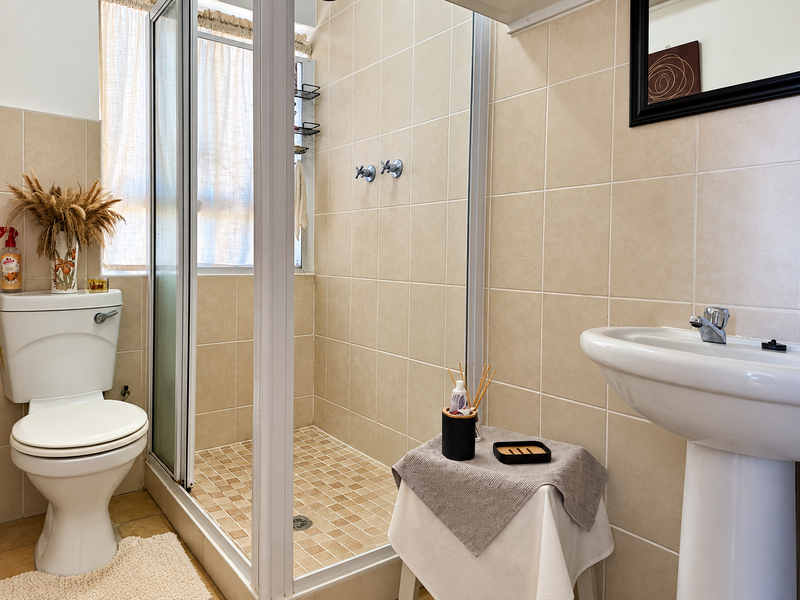 A functional bathroom featuring a shower enclosure, pedestal basin, and toilet with neutral wall and floor tiling.