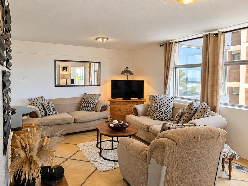A bright and comfortable living room featuring large windows that provide natural light and tiled flooring throughout the space.