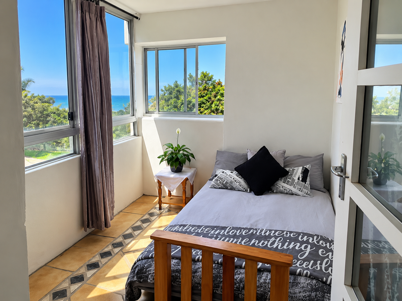 A bright bedroom featuring large windows with ocean views, tiled flooring with a decorative border, and ample natural light.
