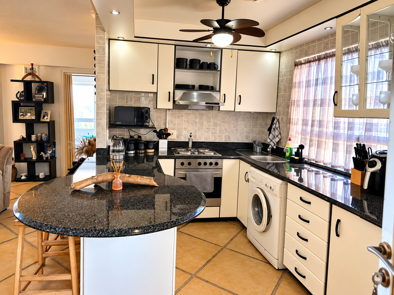 A well-maintained kitchen featuring granite countertops, built-in cabinetry, a gas hob with extractor, and an integrated washing machine, offering a functional and practical layout.