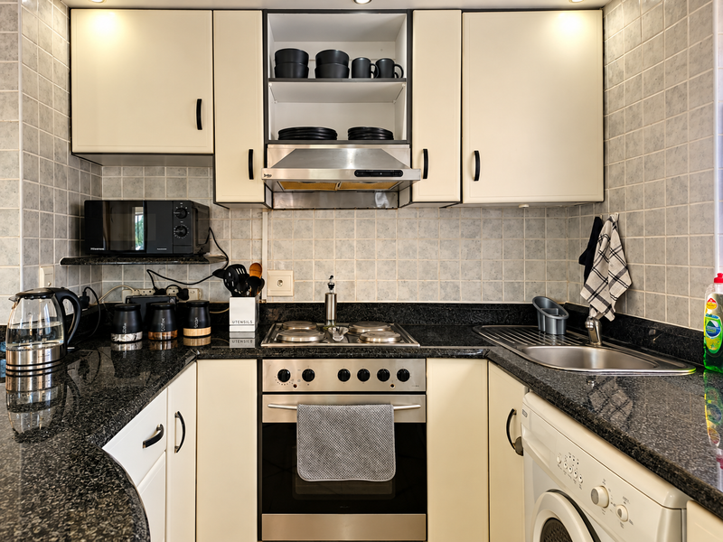 A compact, functional kitchen featuring granite countertops, a built-in oven with gas hob, stainless steel extractor fan, and integrated laundry facilities.