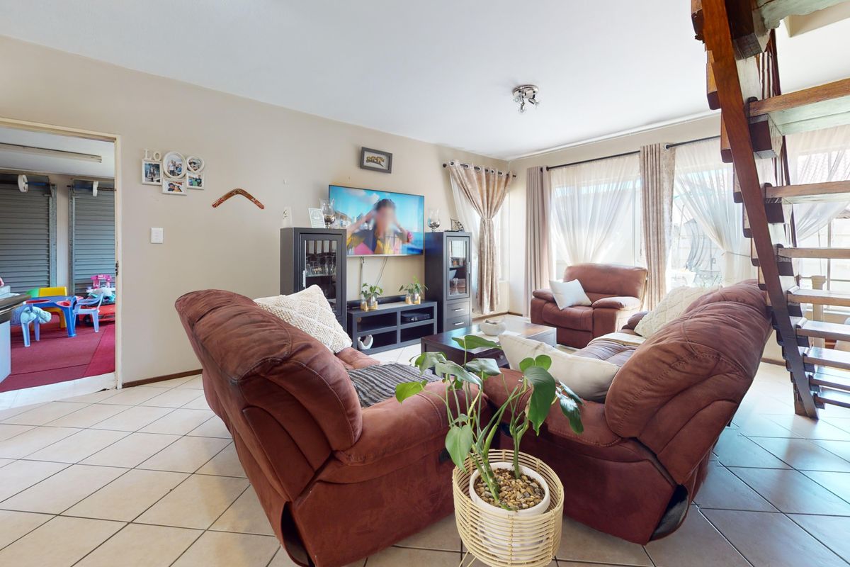 A comfortable living room featuring tiled flooring, a wooden staircase, and access to an outdoor area through a sliding glass door.