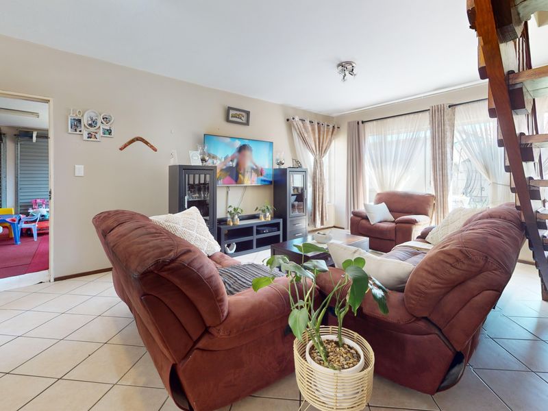 A comfortable living room featuring tiled flooring, a wooden staircase, and access to an outdoor area through a sliding glass door.