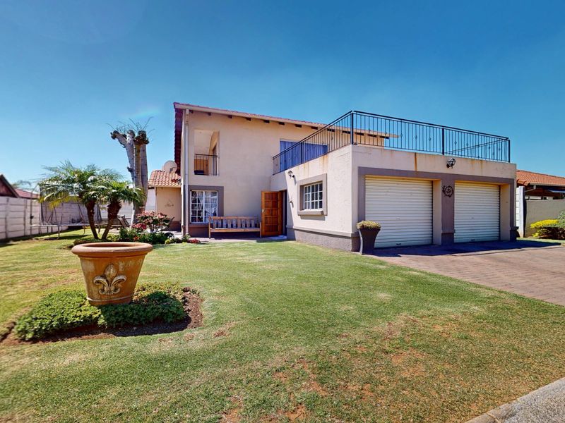 Front view of a double-story cluster home featuring a double garage, paved driveway, manicured lawn, and an upper-level balcony with metal railings.