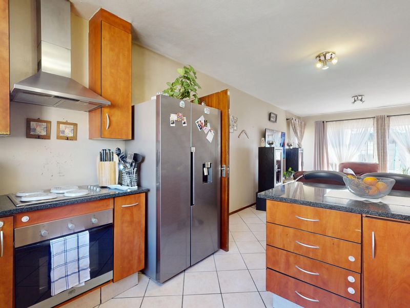 Open-plan kitchen and living area featuring wooden cabinetry, granite countertops, built-in oven, hob, extractor fan, and tiled flooring throughout.
