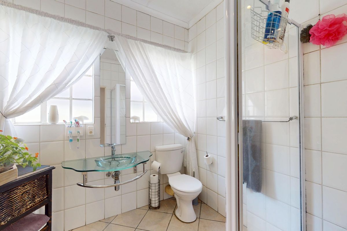 A functional bathroom featuring a glass vessel sink, a toilet, and a shower enclosure with white tiled walls and neutral floor tiles.