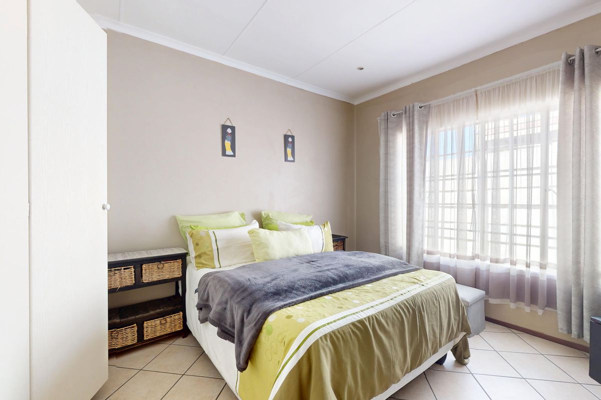 A well-lit bedroom featuring tiled flooring, a built-in wardrobe, and a window fitted with security bars.
