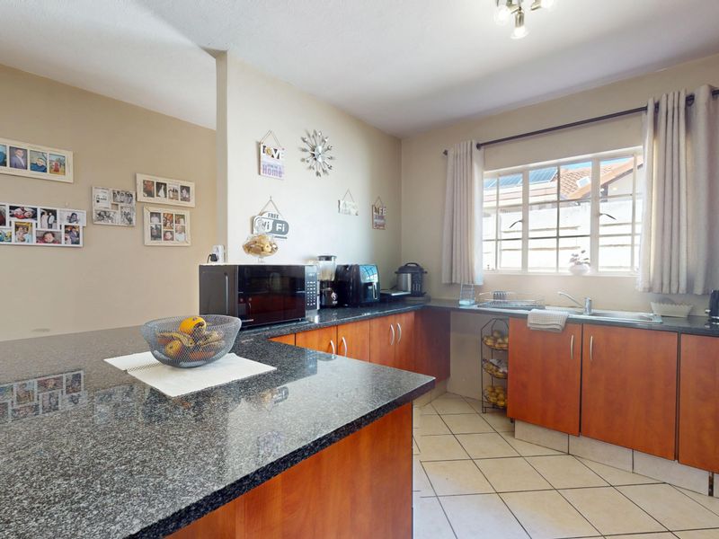 A functional kitchen featuring granite countertops, wooden cabinetry, and tiled flooring, offering a practical layout with a breakfast bar and ample storage space.